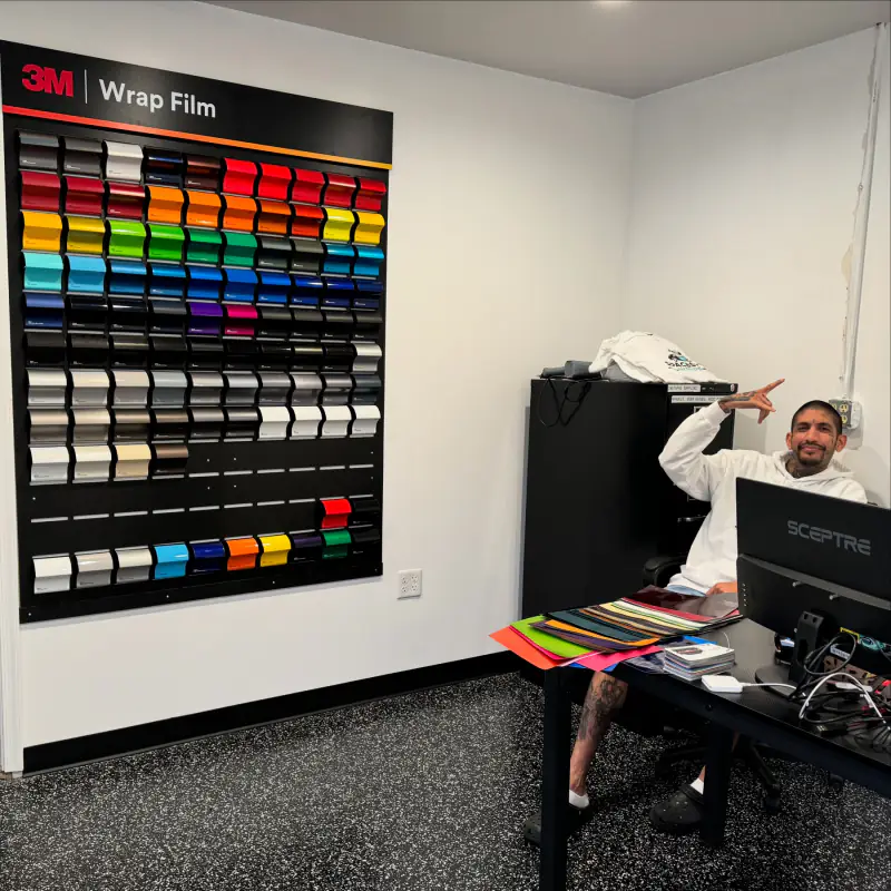 The 3M Wrap Film sample board mounted on the wall, with loose color swatches spread across the desk beside it