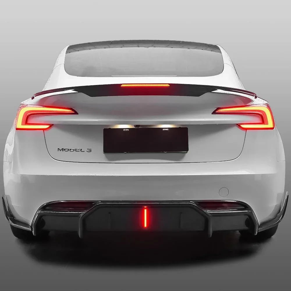 The rear of a white Tesla Model 3 head-on with a black lip spoiler fitted across the trunk lid, its LED strip lit red, and a separate black rear diffuser below the bumper also lit