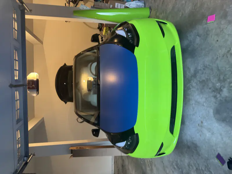 A Tesla part-way through a lime green wrap inside a residential garage, with film leaning against the wall