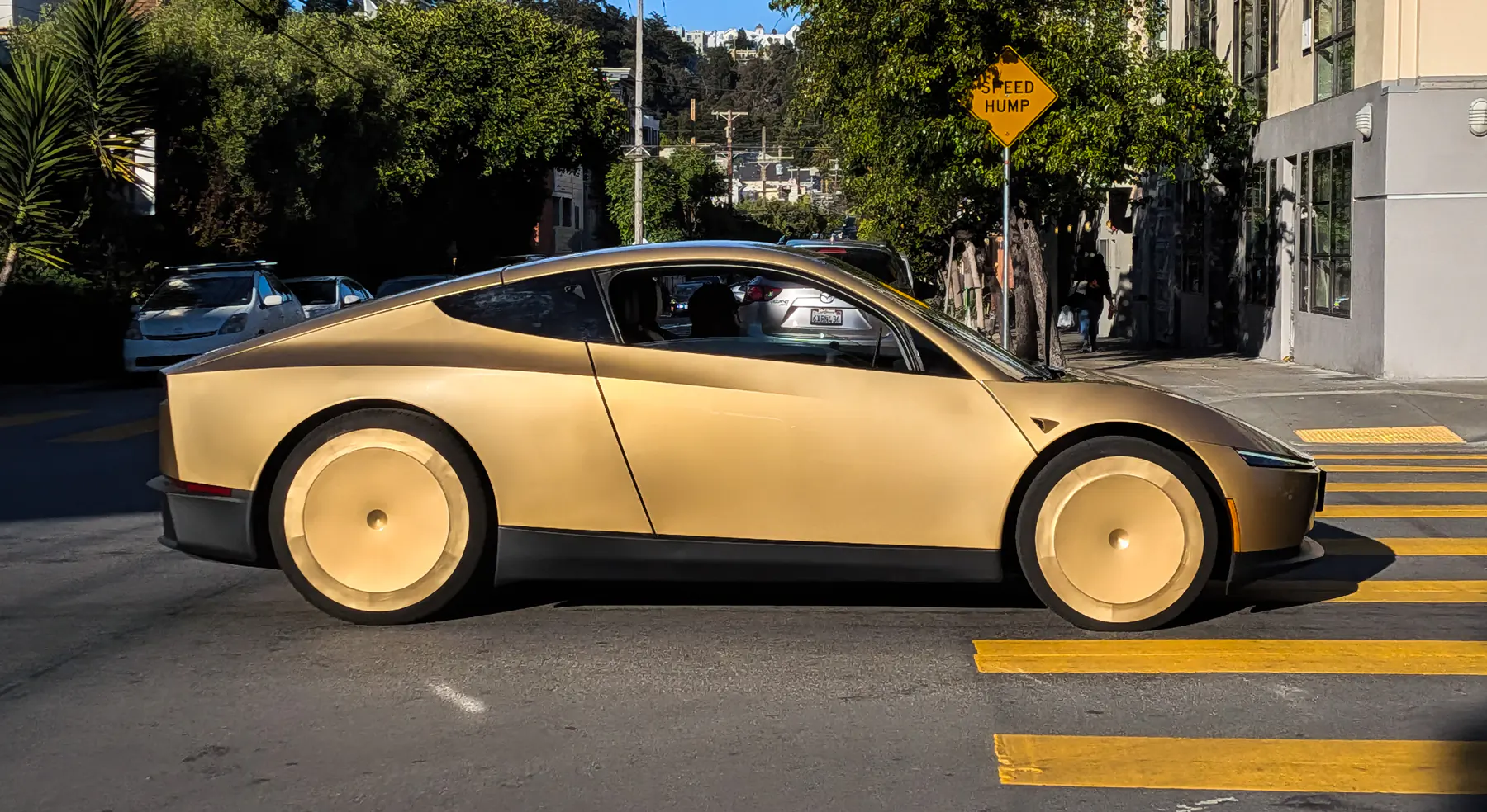 A Tesla Cybercab in its factory gold finish, photographed in profile on a street in San Francisco