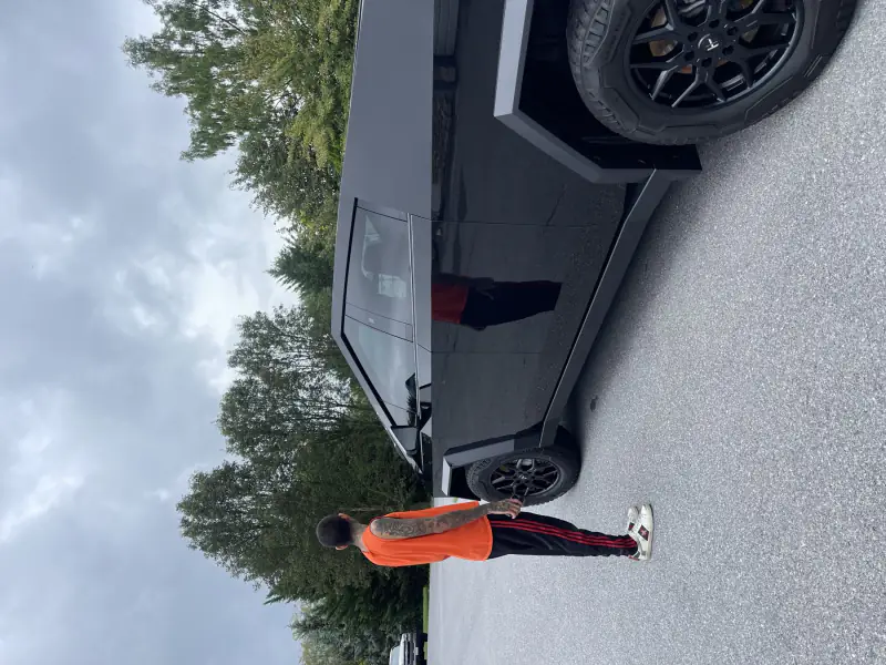 An installer standing beside a Cybertruck wrapped in gloss black, checking the finish