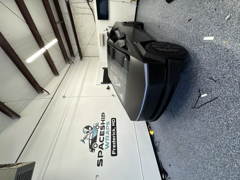 Matte black Cybertruck finished in the bay, beside the Tesla Wrapper wall logo