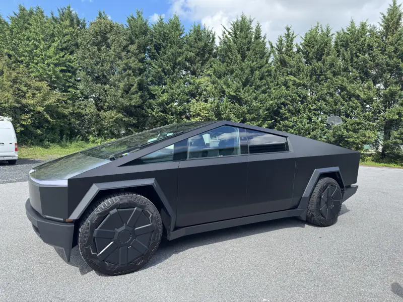 Cybertruck in a matte black wrap, three-quarter view outside the bay