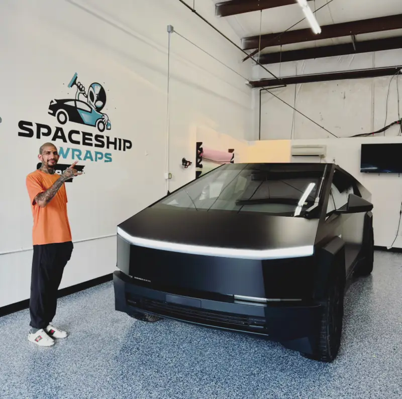 A Cybertruck in satin black finished in the bay, with a member of the shop standing beside it