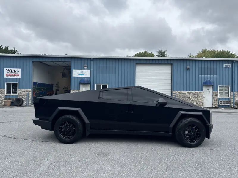 Full side profile of a Cybertruck wrapped in black, outside the bay