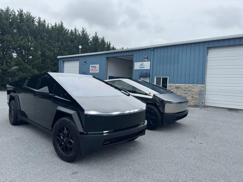 A Cybertruck wrapped in gloss black parked beside one still in bare stainless