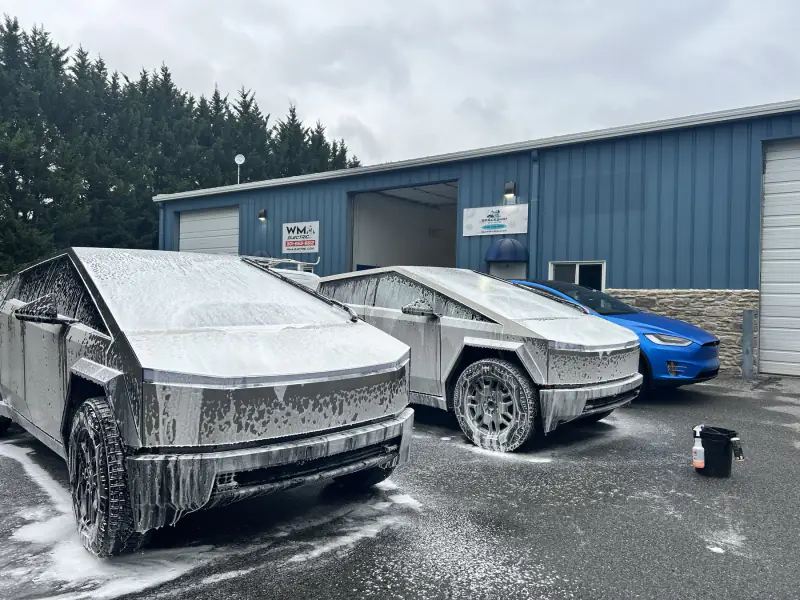 Two Cybertrucks covered in wash foam outside the bay, being decontaminated before any film goes on