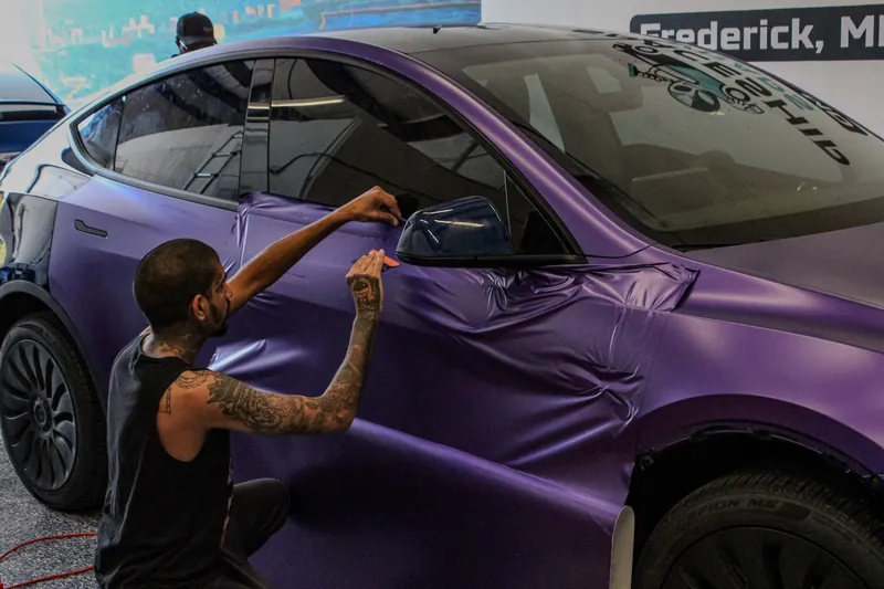 Installer squeegeeing purple satin film onto the rear quarter of a Tesla inside the shop