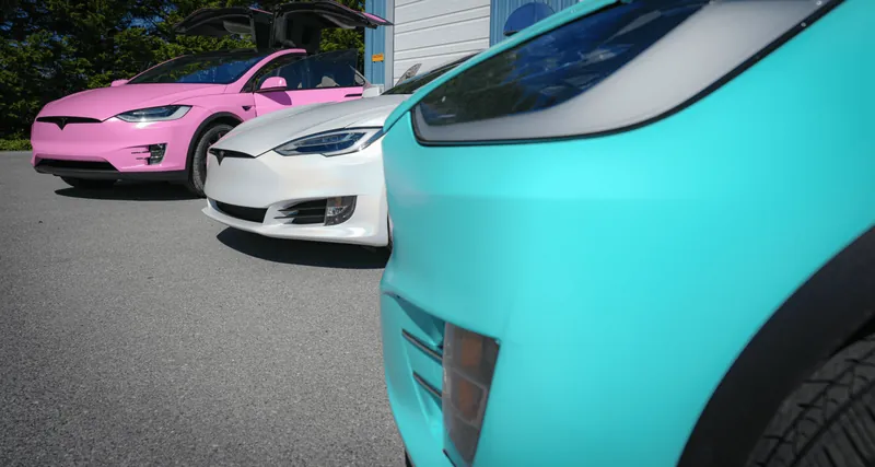 Three wrapped Teslas lined up — pink Model X, satin white Model S, and a teal car