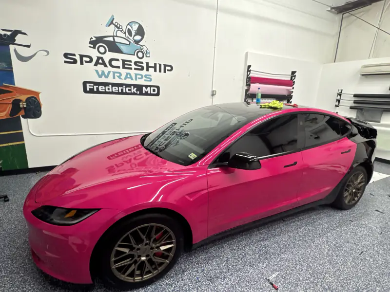 Hot pink Model 3 finished in the bay beside the Tesla Wrapper Frederick wall logo