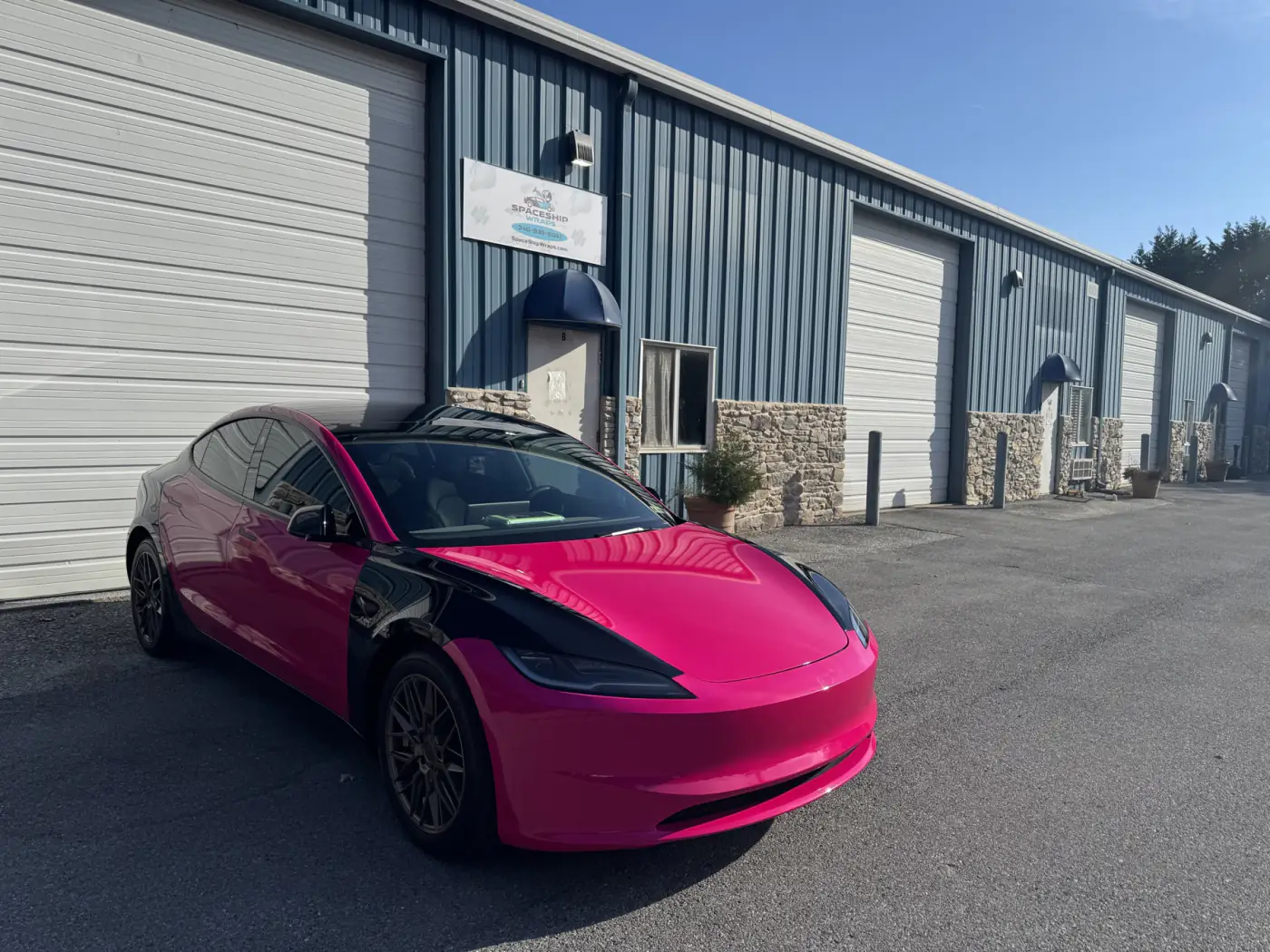 Tesla Model 3 in hot pink with a black hood flash and black roof, outside the bay