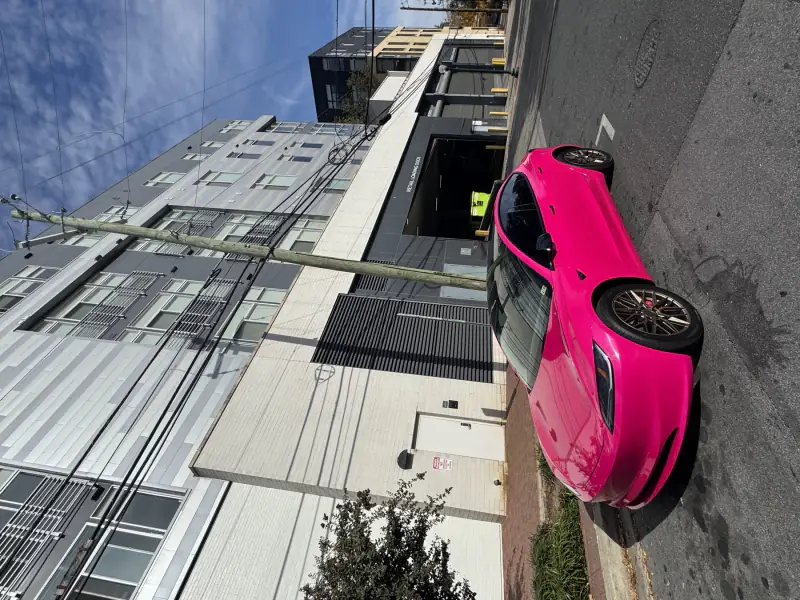 Tesla Model 3 wrapped in hot pink, parked on a city street in the sun