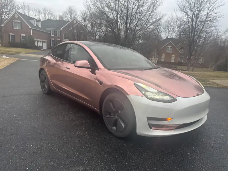 Model 3 in rose gold chrome with the front bumper not yet wrapped, on a driveway