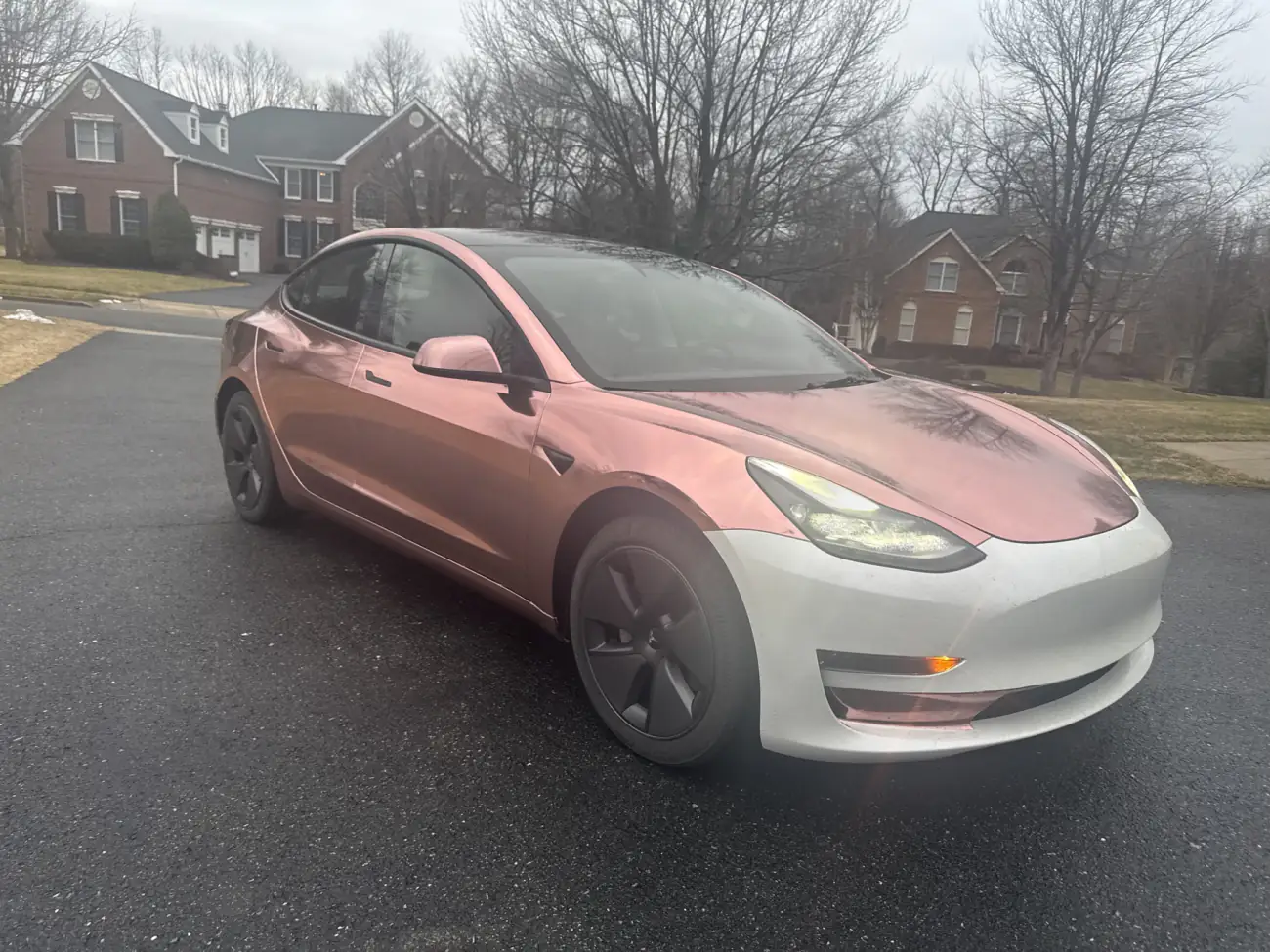 Model 3 in rose gold chrome with the front bumper not yet wrapped, on a driveway
