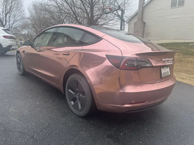 Rear three-quarter of a Model 3 in rose gold chrome, carrying a decal for ModelWrapped, the shop’s earlier name