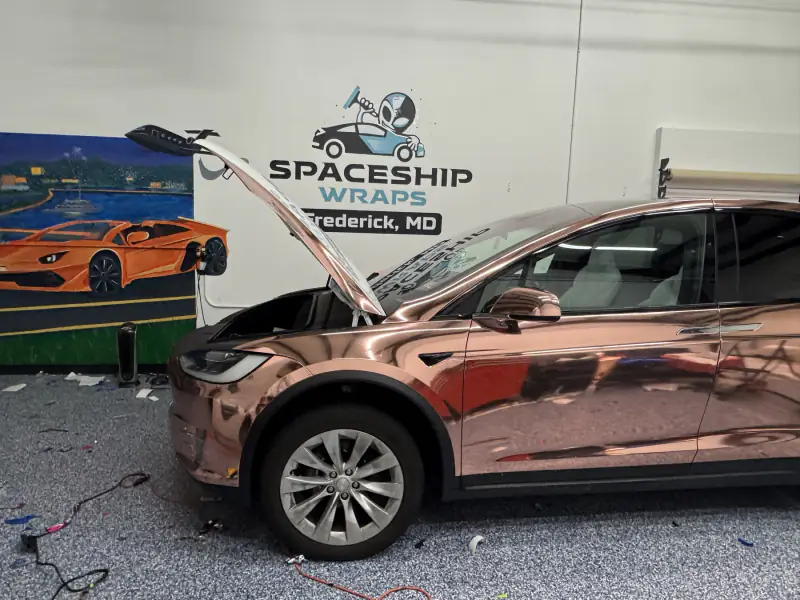 Model X in rose gold chrome with the hood raised, in the bay