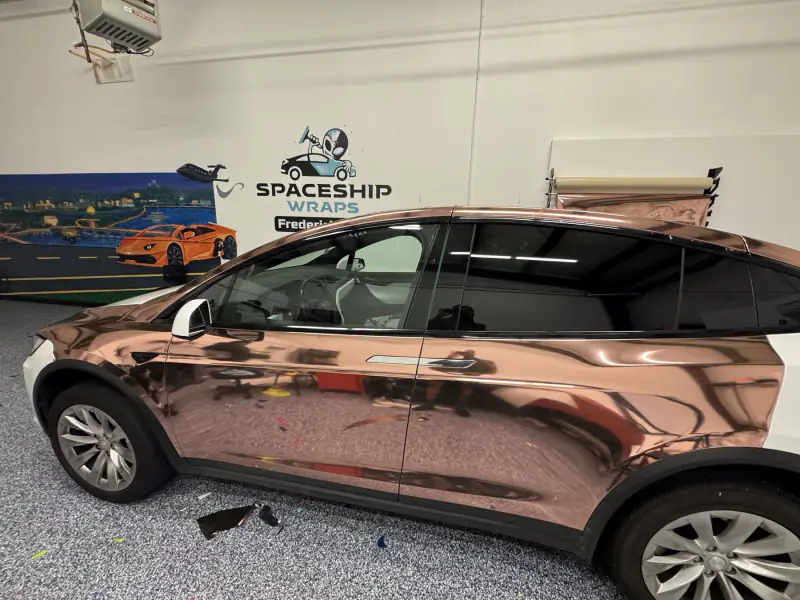 Rose gold chrome film laid across the doors of a Model X, reflecting the shop floor