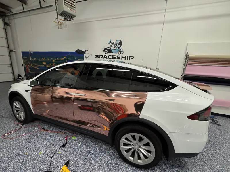Model X half-wrapped in rose gold chrome — the doors finished, the rear quarter still factory white