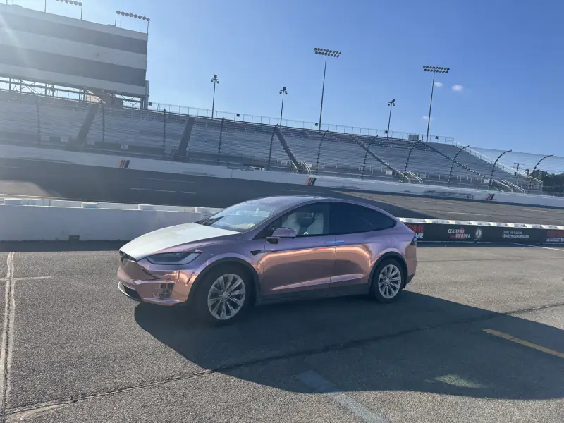 Model X in rose gold chrome with a white nose, parked on a race track apron