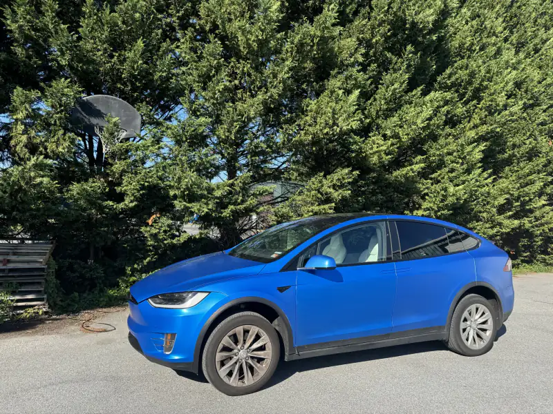 Tesla Model X wrapped in a satin blue, parked outside with the factory wheels left as they were