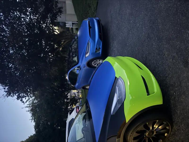 A lime green and blue Tesla beside a satin blue Model X at dusk