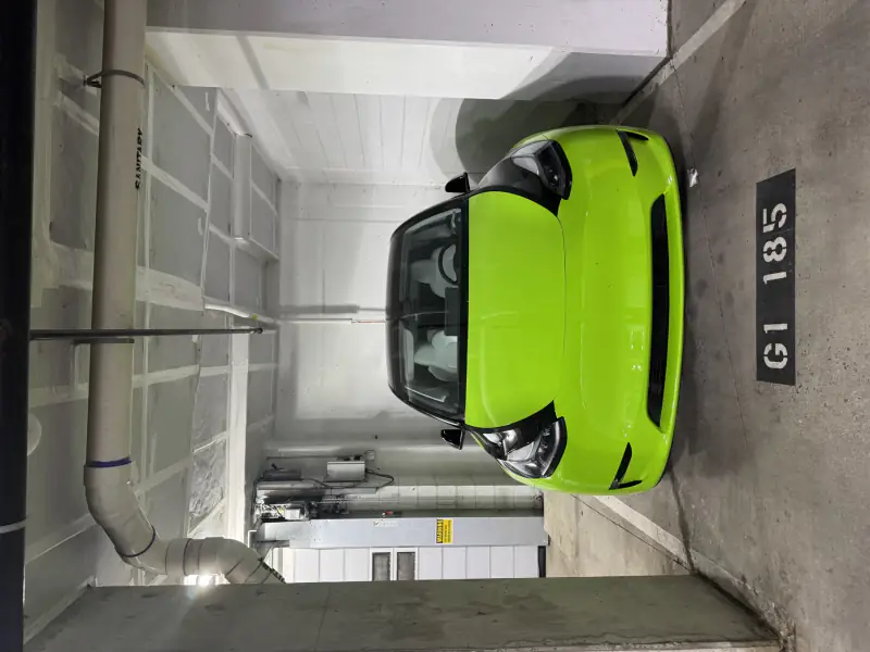 Tesla Model Y finished in lime green with a black roof and hood, parked in a garage