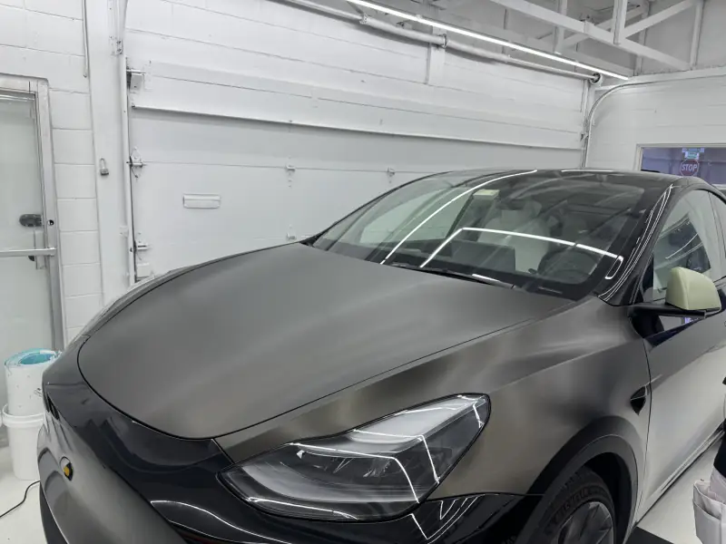 Hood and A-pillar of a Tesla wrapped in satin graphite, film cut clean along the windscreen edge