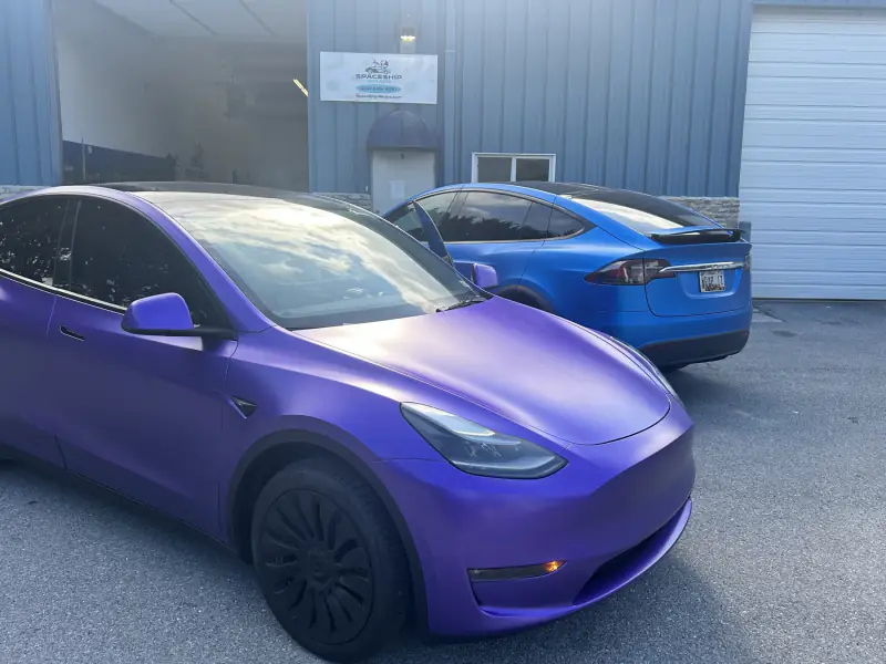 Tesla Model Y in satin purple outside the bay, with a satin blue Model X behind it