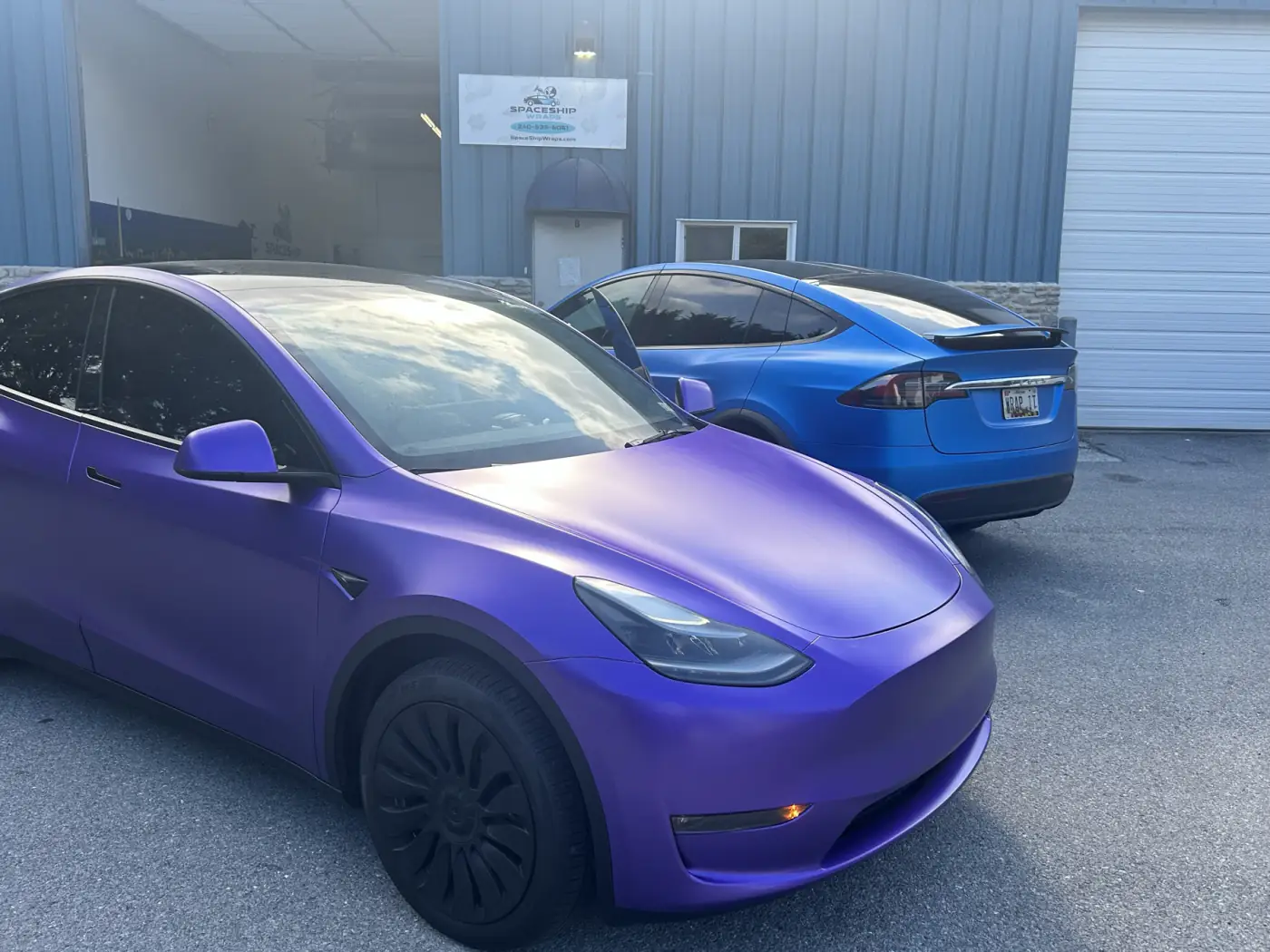 Tesla Model Y in satin purple outside the bay, with a satin blue Model X behind it