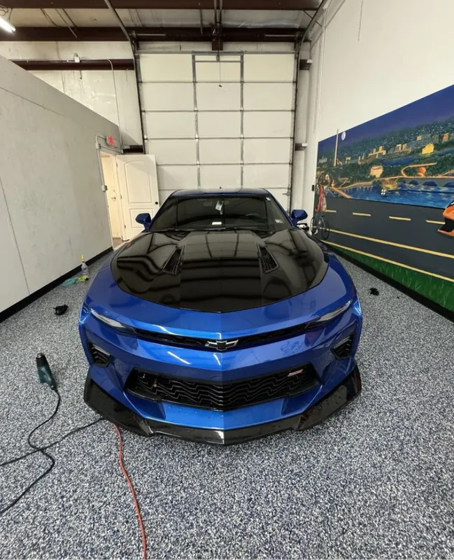 Muscle car wrapped in a blue color-shift film, front view under shop lighting
