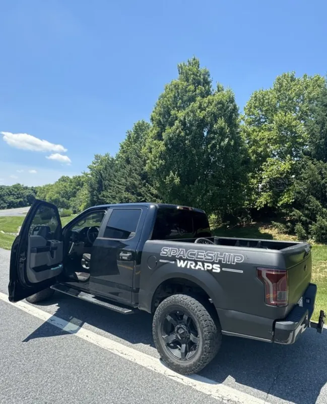 Satin black pickup truck carrying Tesla Wrapper branding, doors open outside the shop