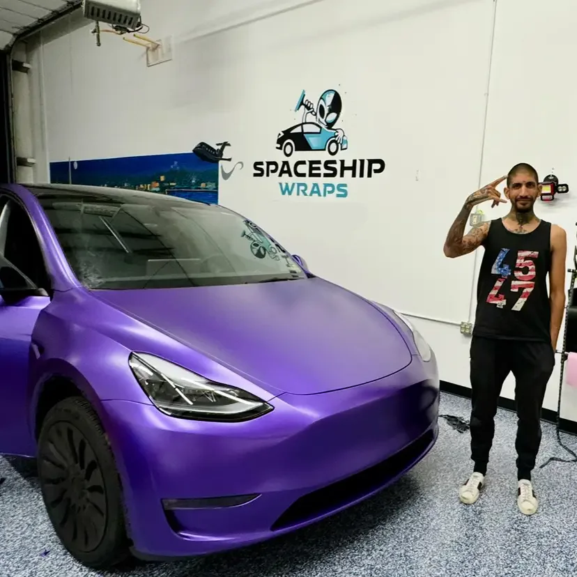 Raoul Shah standing beside a Tesla Model Y finished in satin purple, in the installation bay