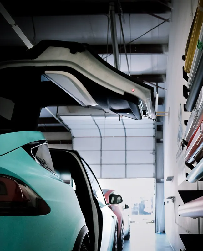 Rack of vinyl film rolls on the shop wall above a wrapped car