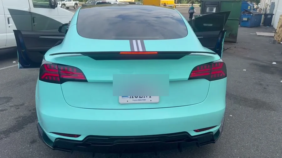 The rear of the Model 3 with the LED rear spoiler lit red across the trunk lip; plate blurred