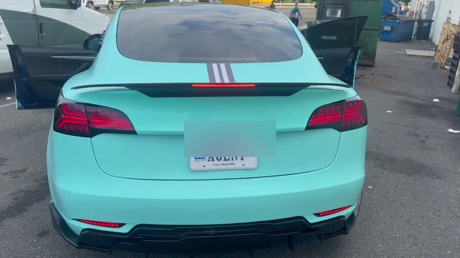 The rear of the Model 3 with the Lamborghini-style tail lights lit, the rear diffuser and the roof-to-trunk stripes visible; plate blurred