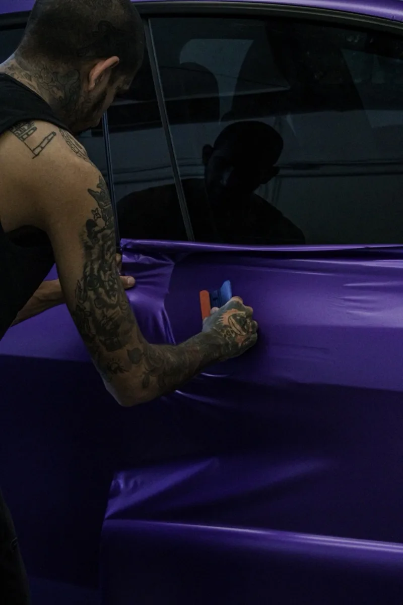 Close view of hands squeegeeing purple film across a Model Y door
