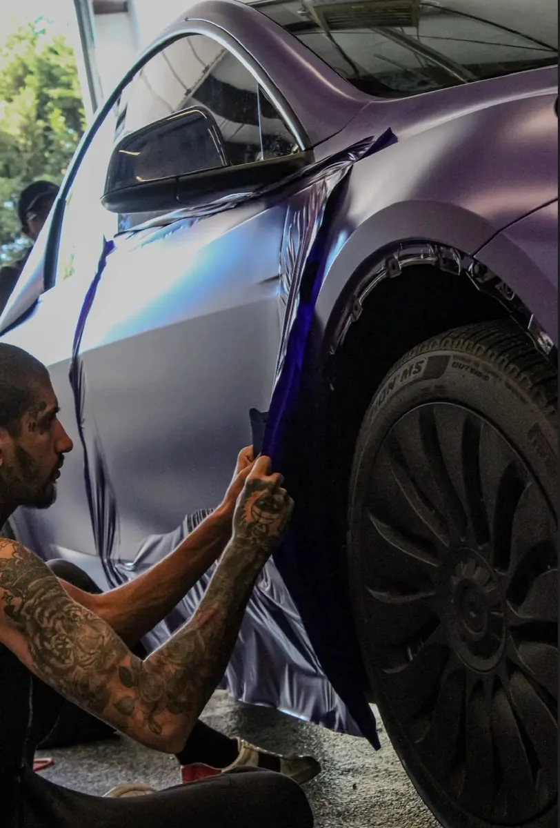 Film being pulled and worked around the rear wheel arch of a Model Y