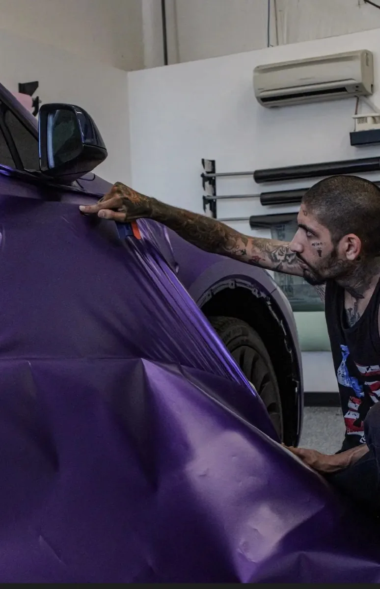 Raoul stretching purple film over the front fender and mirror of a Model Y in the Frederick bay