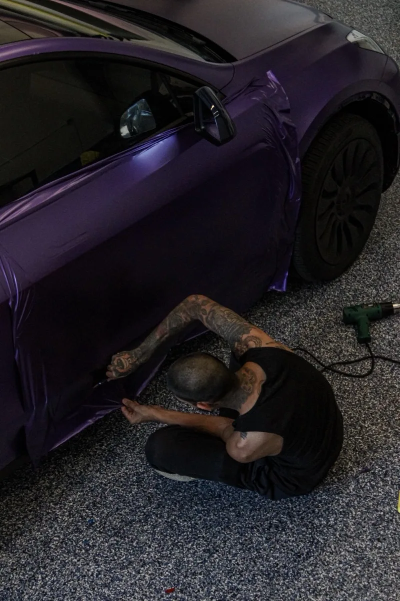 Working the lower rocker of a Model Y from the ground, heat gun beside the car