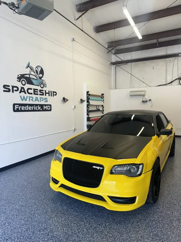 Yellow-wrapped sedan with a gloss black roof inside the Tesla Wrapper install bay